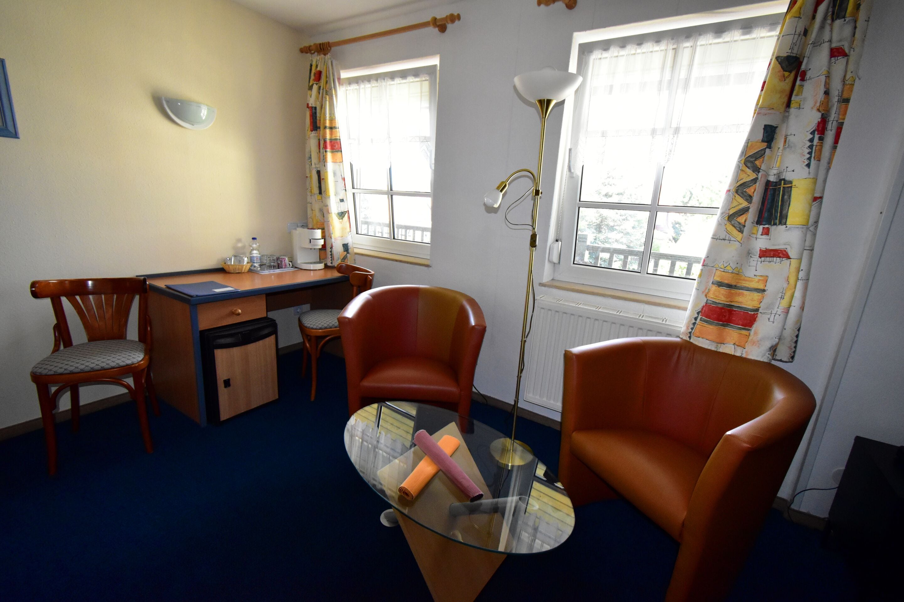 A room with a desk, two chairs, a glass table, and a floor lamp.