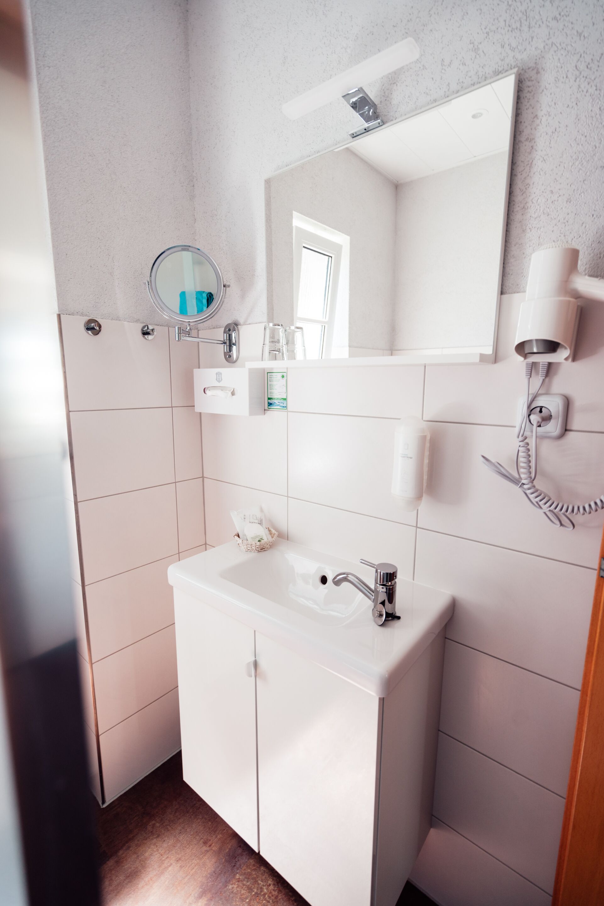 Un baño moderno con un lavamanos blanco, espejo y perchero.