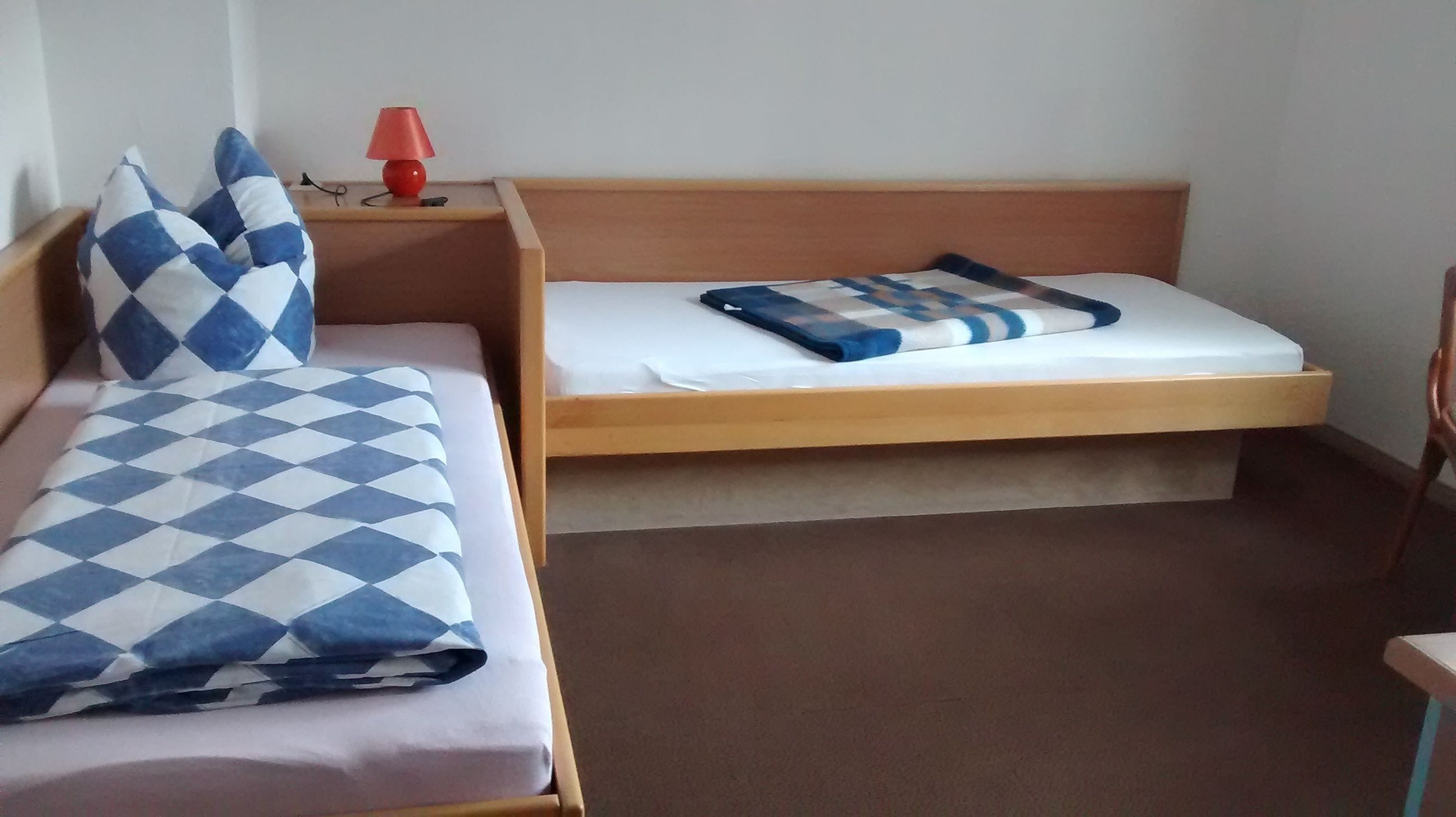 Una habitación con dos literas, una lámpara roja en la mesita de noche y una manta blanca y azul a cuadros sobre una de las camas.