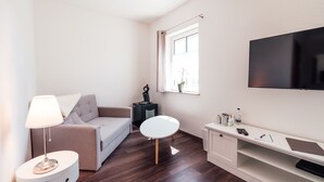 A modern living room with a sofa, a round white table, a lamp, a TV, and a small side table with a plant. - Hotel Garni Rank (Bad Berka)