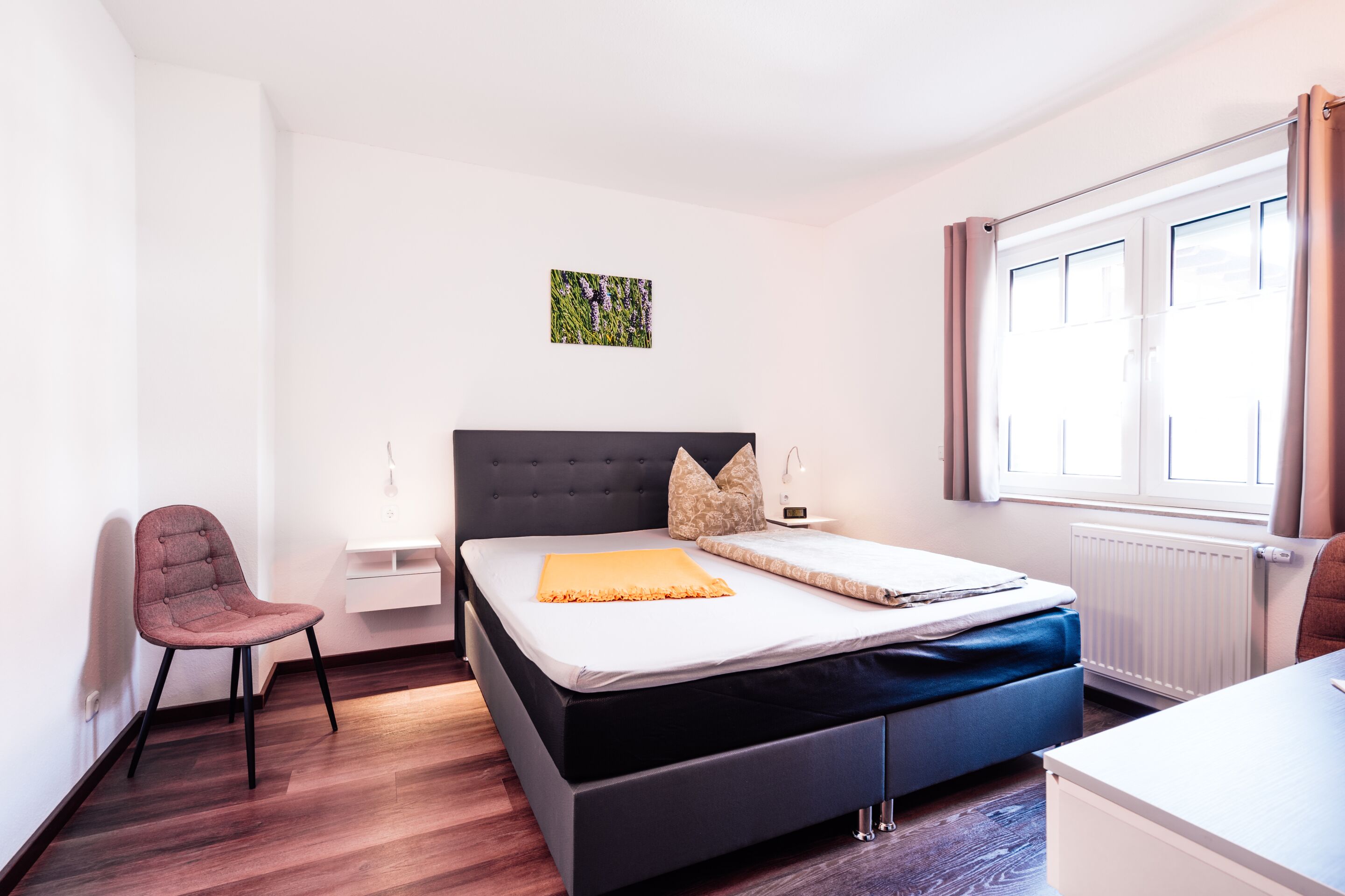 A modern hotel room with a bed, a chair, a desk, and a window.
