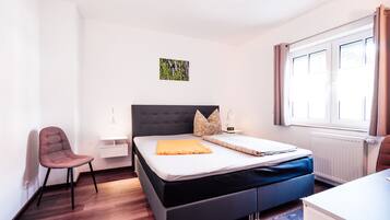 A modern hotel room with a bed, a chair, a desk, and a window.