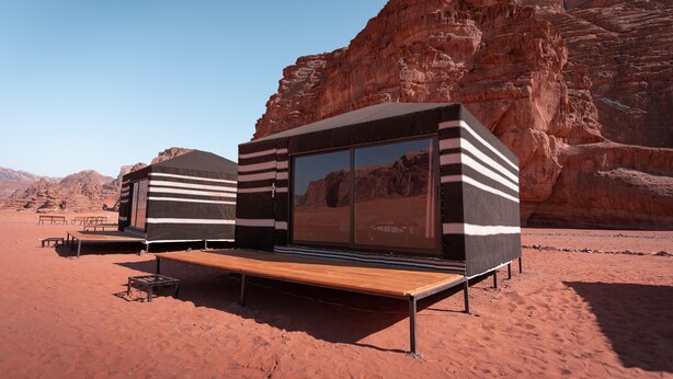 A modern, minimalist structure with a flat roof and large windows, situated in a desert environment with red rock formations in the background. - Desert Bird Camp (Wadi Rum)