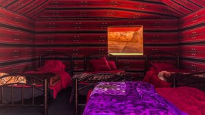 A room with a sloped ceiling, a bed with a purple blanket, and a window with a red curtain. - Desert Bird Camp (Wadi Rum)
