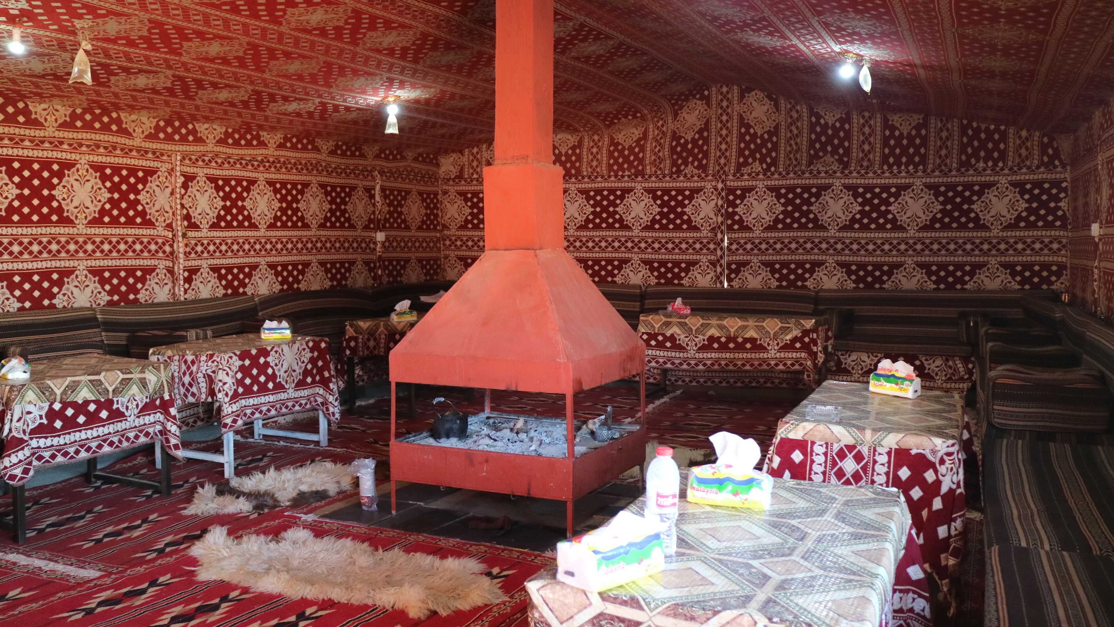 A traditional room with patterned walls, a central red chimney, and multiple tables with patterned tablecloths.