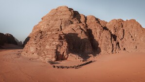 A desert landscape with a prominent rock formation and a series of tents arranged in a line. - Desert Bird Camp (Wadi Rum)