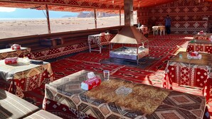 A tented dining area with patterned carpets, a central grill, and tables set for dining. - Desert Bird Camp (Wadi Rum)