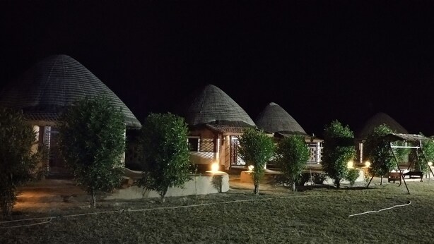 A row of conical-roofed cottages at night, each with a small porch and a bench. - Rann Visamo Village Resort (Bhuj)