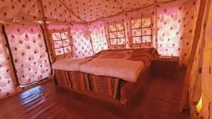 A room with a bed, a small table, and curtains with floral patterns. - Rann Visamo Village Resort (Bhuj)