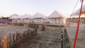 A row of white tents with a dirt ground and a wooden fence in the foreground. - Rann Visamo Village Resort (Bhuj)
