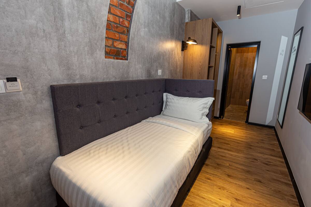 Quarto moderno com cama estofada cinza, parede de tijolos e piso de madeira.