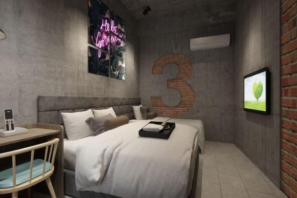 A modern bedroom with a large number '3' on the wall, a bed with white bedding, a desk with a chair, and a neon sign.