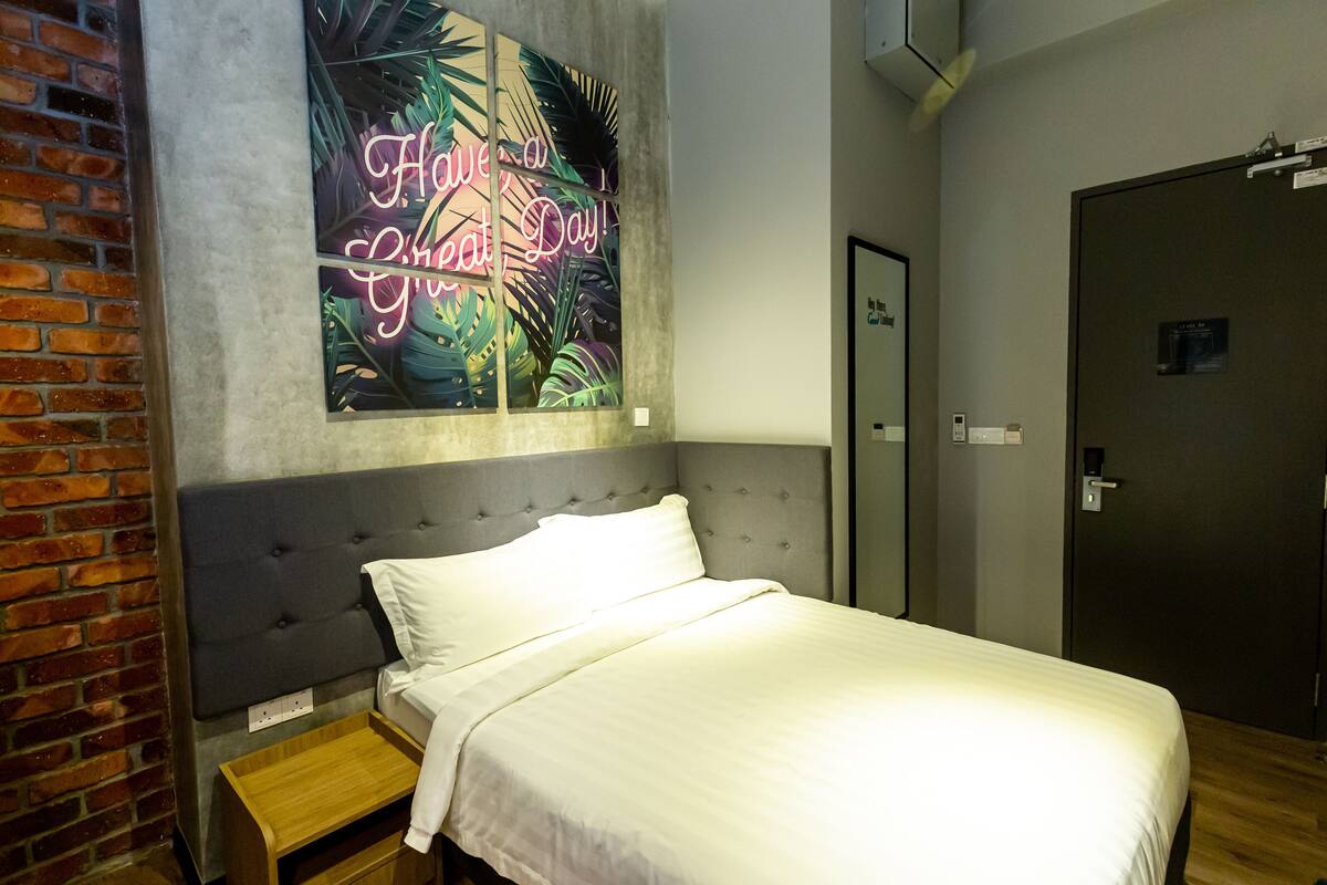 Quarto de hotel com uma cama, mesa de cabeceira, parede de tijolos e um letreiro de neon na parede.