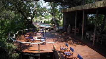 Relax on the deck surrounded by lush greenery, with comfortable seating and a covered dining area.