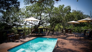 A wooden deck with a swimming pool, outdoor furniture, and umbrellas.