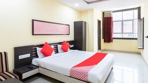 Habitación de hotel con cama, mesita de noche, armario, ventana con cortinas y ventilador de techo.