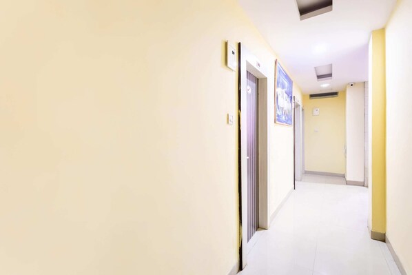 A narrow, well-lit hallway with cream walls and a yellow accent wall, leading to a door with a sign. - OYO 40153 Hotel Rajendra Palace (Ratlam)