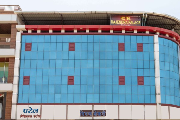 Un hotel con fachada azul, un cartel que indica Rajendra Palace y un anuncio de farmacia.