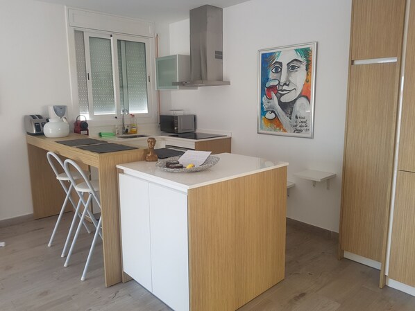 A compact kitchen with a microwave, toaster, and sink. There's a small island with a paper and a banana. A chair is next to the island.
