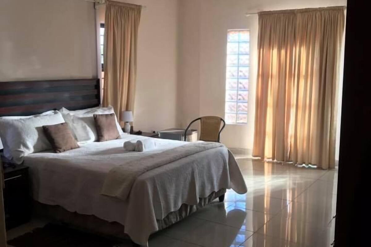 A spacious hotel room with a large bed, a chair, and a window with curtains.
