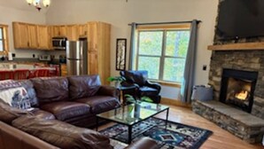 A living room with a leather sofa, a glass coffee table, and a fireplace. - Foothills Family Retreat - Hot Tub and Fire Pit (Dahlonega)