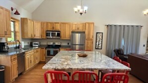 A kitchen with wooden cabinets, a granite island, red chairs, and a chandelier. - Foothills Family Retreat - Hot Tub and Fire Pit (Dahlonega)