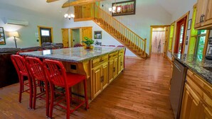 A spacious kitchen with a central island, wooden cabinets, and a staircase leading to an upper level. - Foothills Family Retreat - Hot Tub and Fire Pit (Dahlonega)