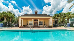 A pool area with a covered seating area, a lifeguard stand, and a clear blue sky. - ✦Best Deal✦Cozy Home w/ WiFi, Baby Gear, 6mi to Disney, Onsite Theatre/Pool✦ (Kissimmee)