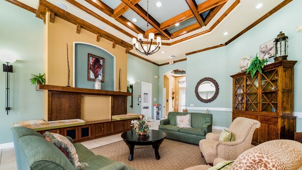 A spacious living room with a high ceiling, wooden beams, a fireplace, and a large mirror. - ✦Best Deal✦Cozy Home w/ WiFi, Baby Gear, 6mi to Disney, Onsite Theatre/Pool✦ (Kissimmee)