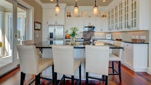 Une cuisine moderne avec des meubles blancs, un îlot central doté de tabourets et des luminaires suspendus.