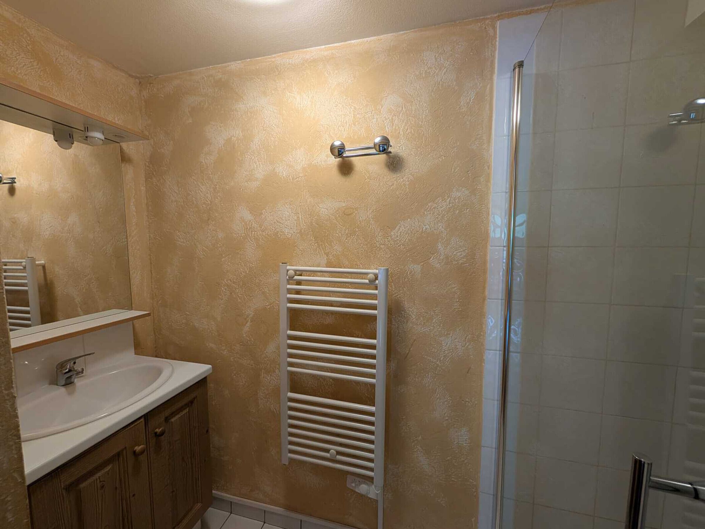 A bathroom with a white sink, wooden cabinets, a white towel rack, and a glass shower enclosure.