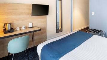 A hotel room with a bed, a desk with a chair, a TV mounted on the wall, and a mirror.