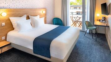 A hotel room with a large bed, a desk with a chair, a TV, and a view of the outdoors.