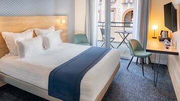 A hotel room with a large bed, a desk with a chair, a TV, and a balcony with a table and chairs.