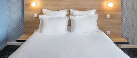 Una cama bien tendida con sábanas blancas y un detalle azul al pie.