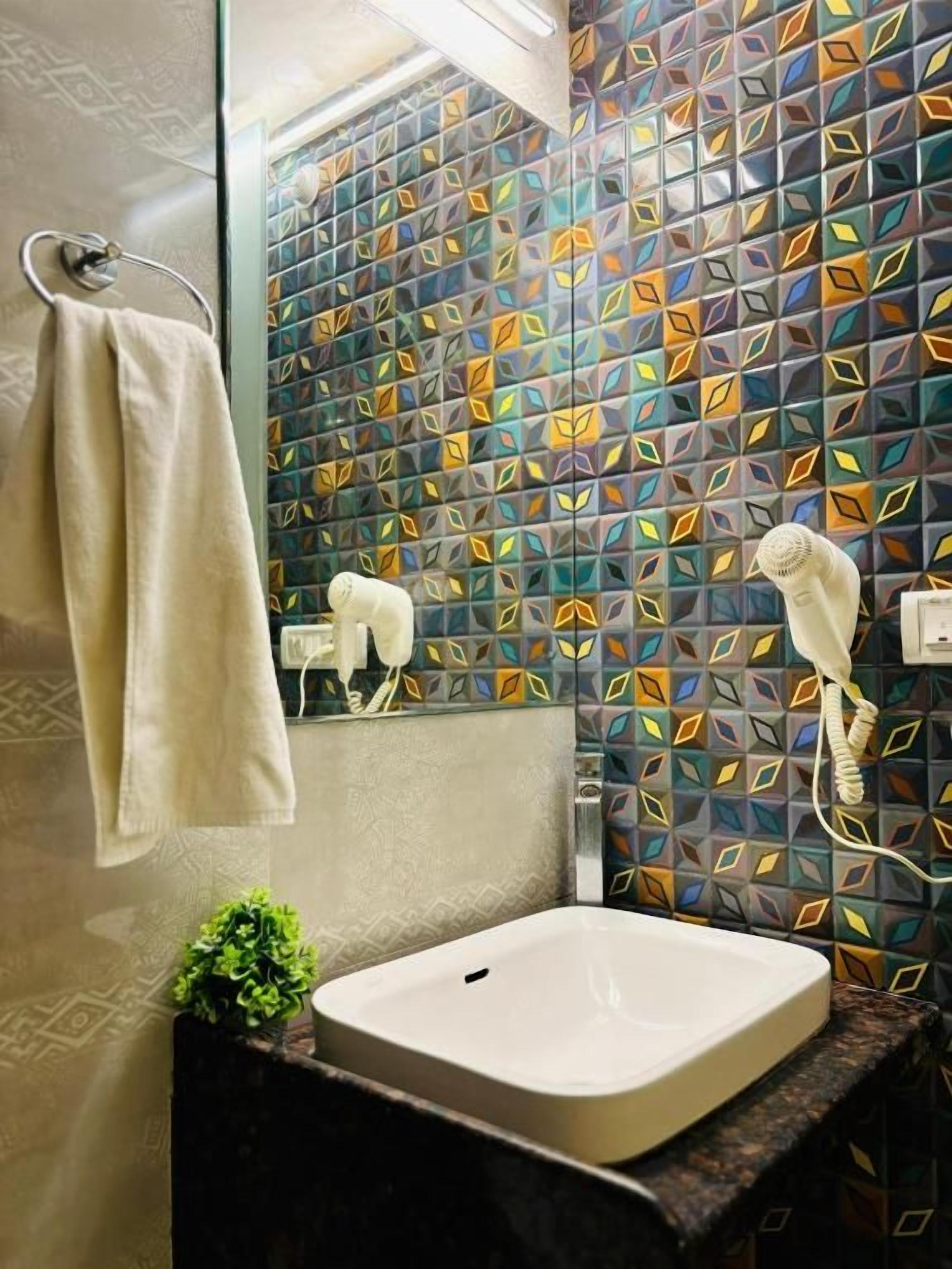 A bathroom with a patterned tile wall, a sink, a towel rack, and a hairdryer.
