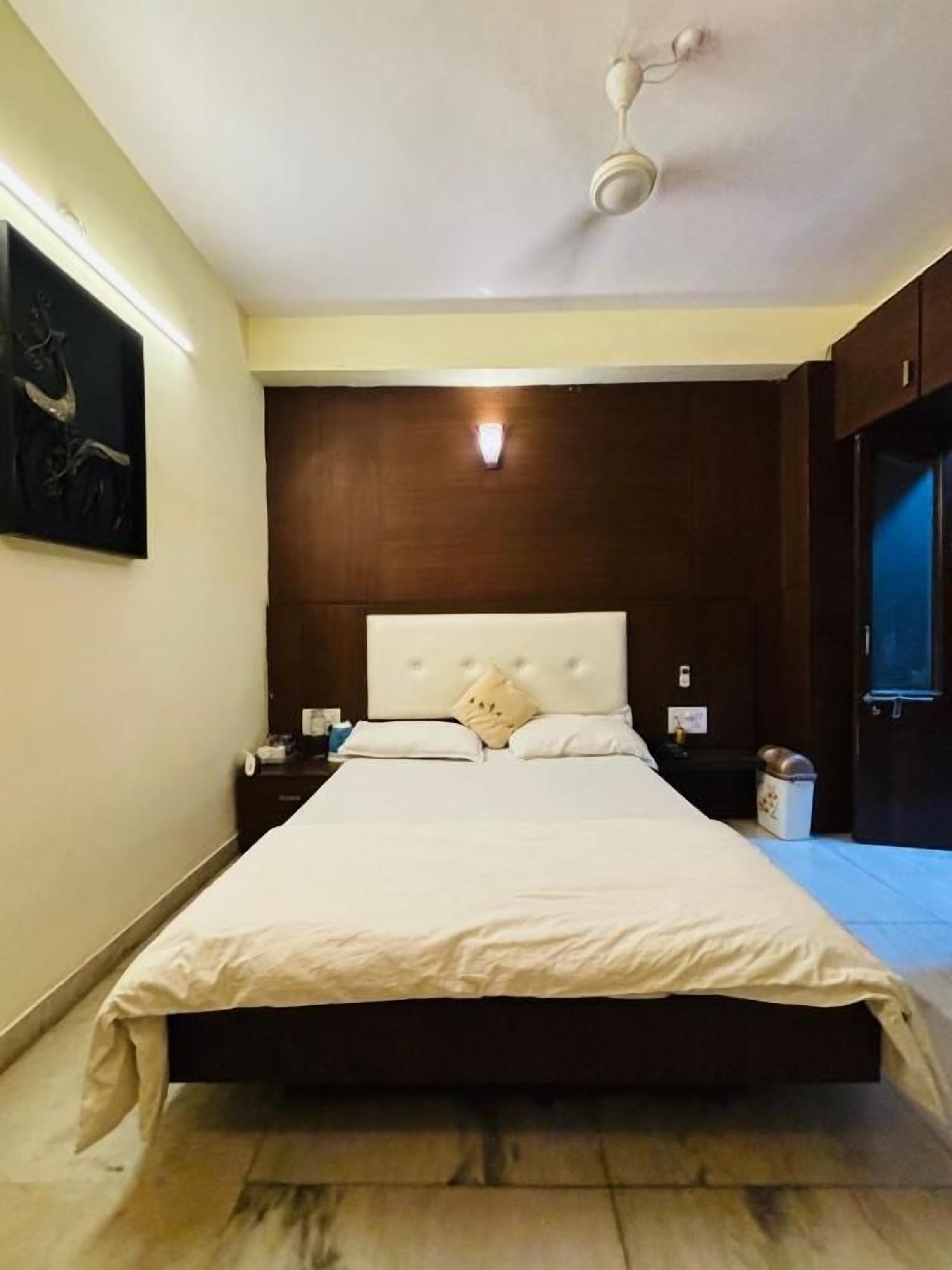 A bedroom with a large bed, a ceiling fan, a nightstand, and a wall-mounted light.