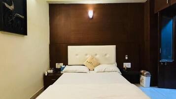 A bedroom with a large bed, a ceiling fan, a nightstand, and a wall-mounted light.
