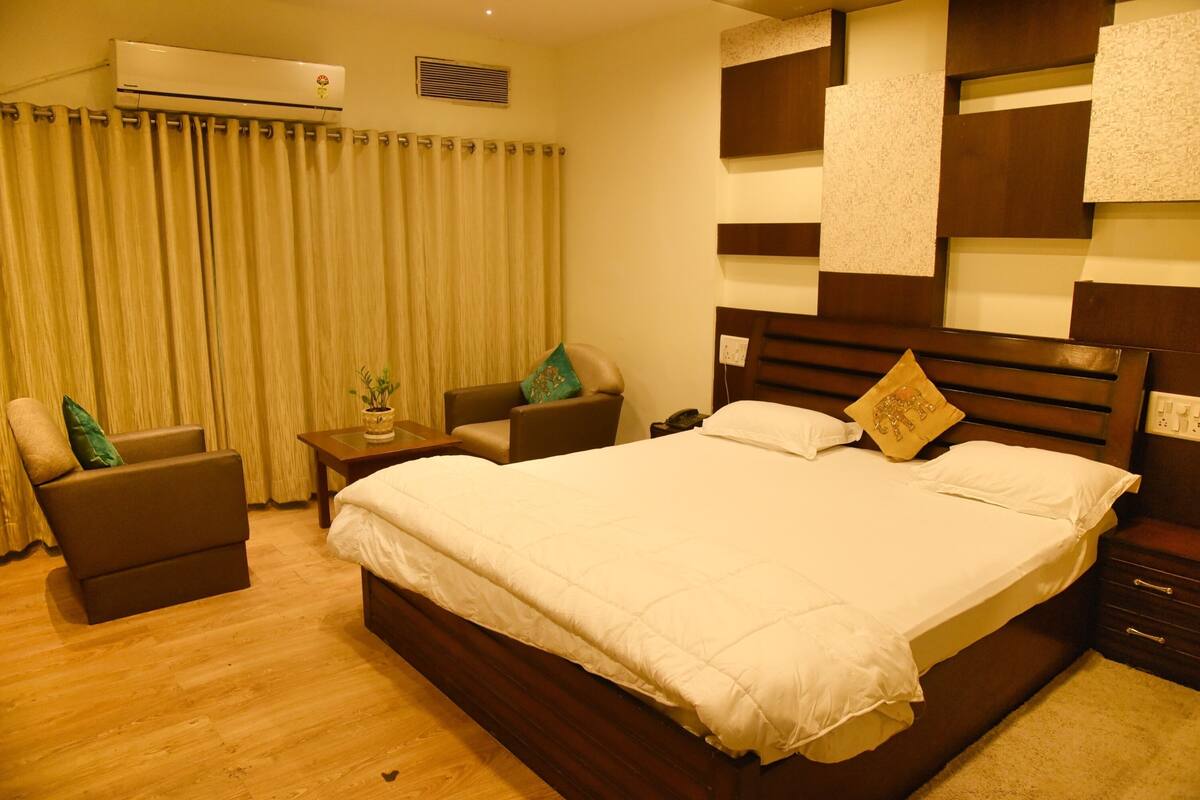 Quarto de hotel com uma cama grande, um sofá, uma mesa de cabeceira e ar condicionado fixado na parede.