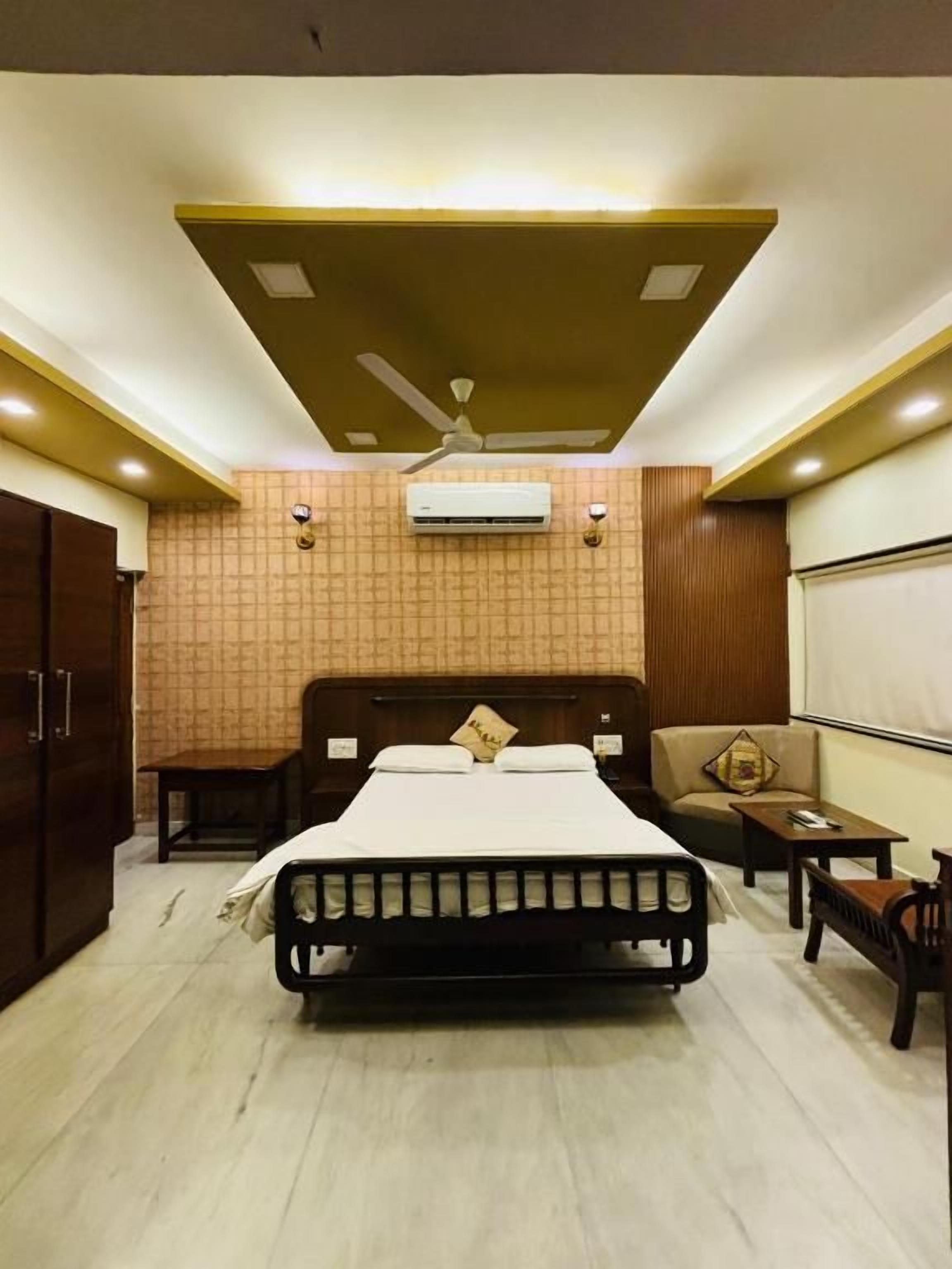Een slaapkamer met een bed, een plafondventilator, een bank, een kleine tafel en een airconditioning.