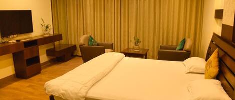 Habitación de hotel con una cama grande, dos sillones, una mesita, un televisor y un equipo de aire acondicionado.