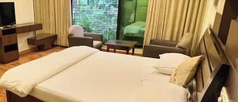 Habitación de hotel con una cama grande, televisión, escritorio y ventana con cortinas.