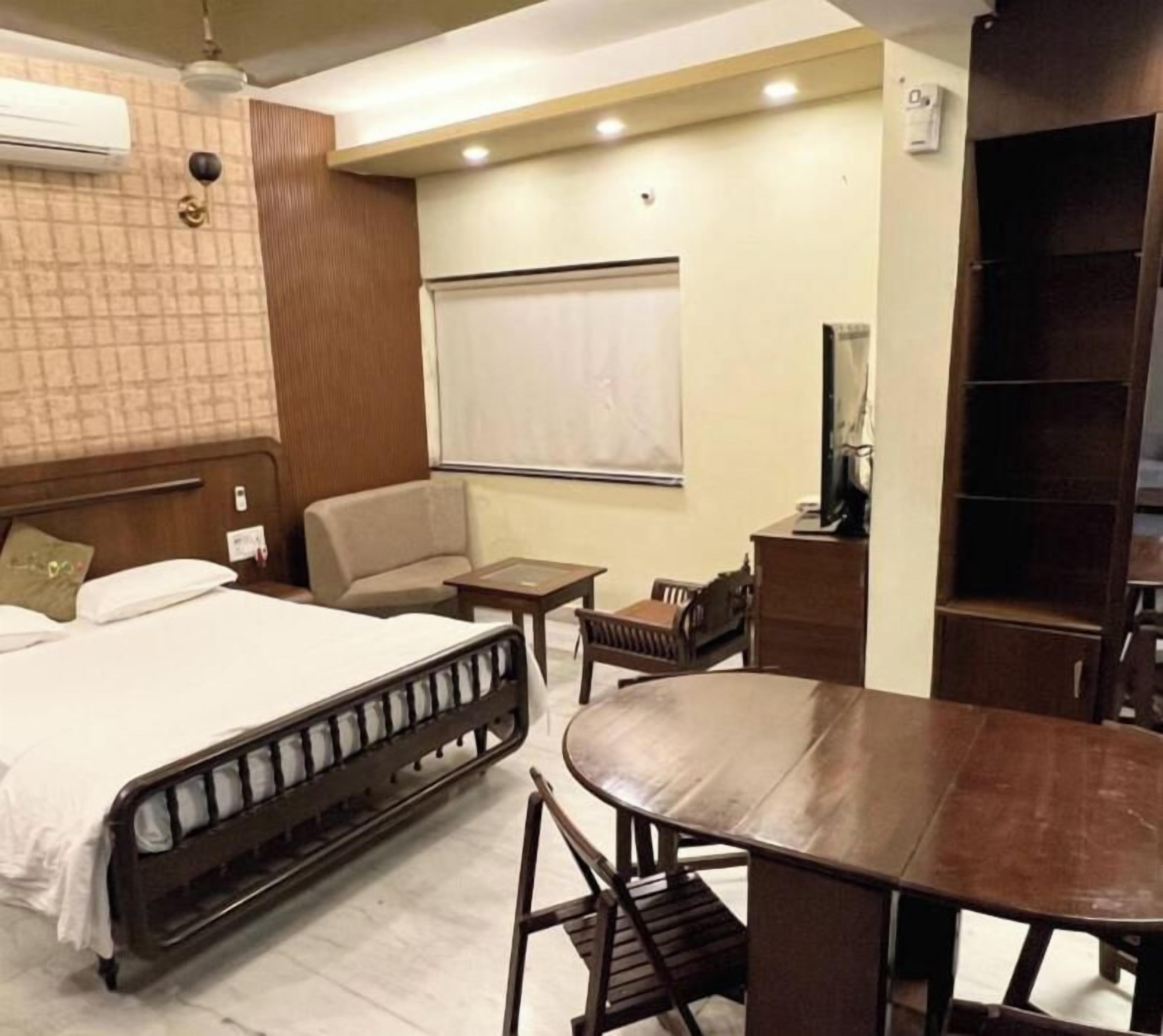 A hotel room with a bed, a dining table, a chair, a small table, and a wardrobe.