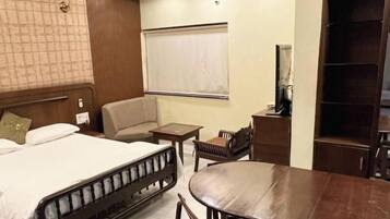 A hotel room with a bed, a dining table, a chair, a small table, and a wardrobe.