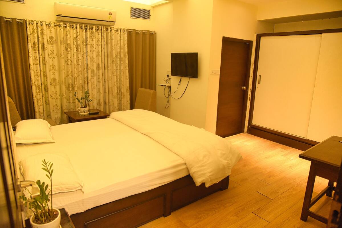 Quarto de hotel com uma cama, mesa de cabeceira, televisão na parede e um guarda-roupa.
