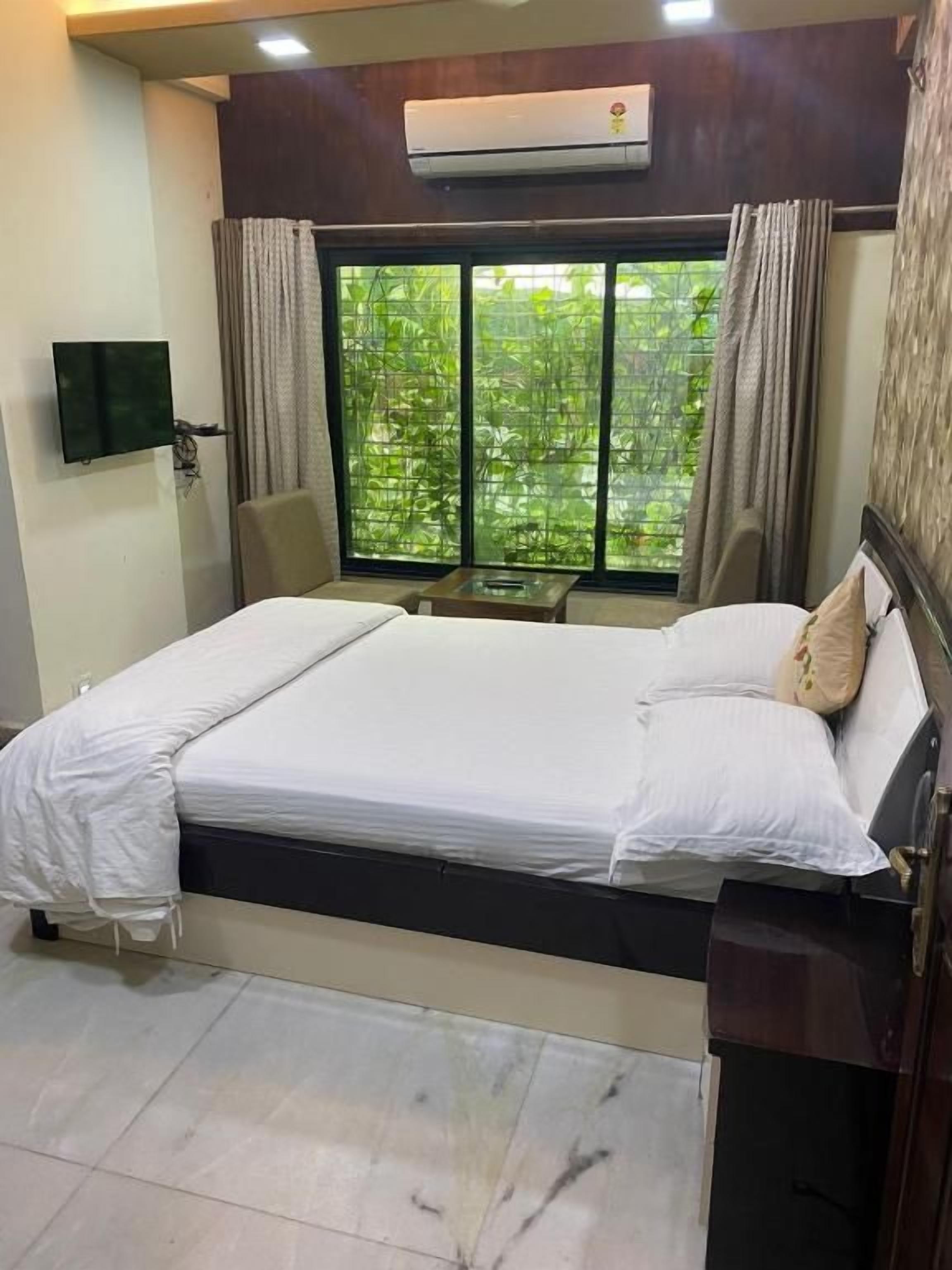 Una habitación de hotel con cama, televisión, ventana con cortinas y aire acondicionado.