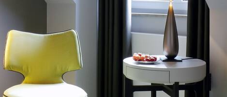 Una habitación con una silla amarilla, una mesita redonda con una lámpara y una cama.