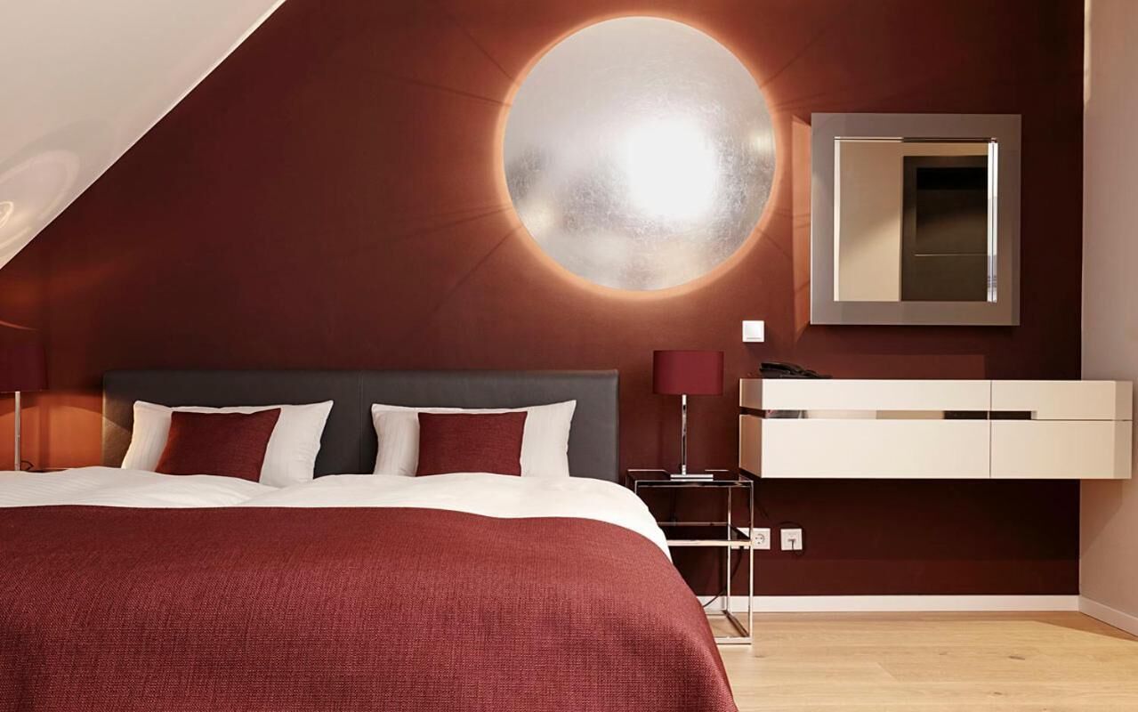 Un dormitorio moderno con una cama grande, una lámpara de pared redonda, un espejo y un tocador blanco.