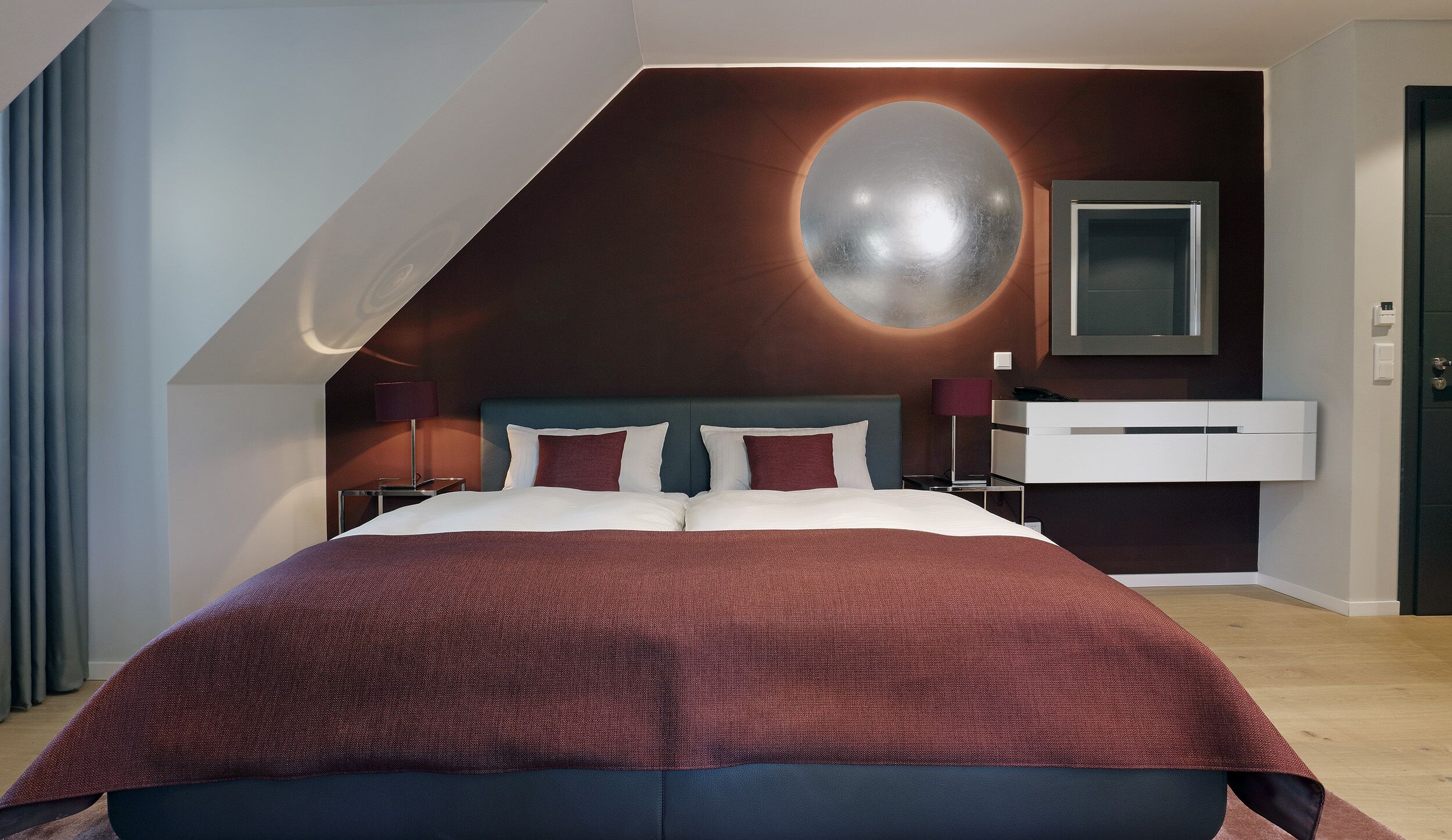 A modern bedroom with a large bed, a nightstand, a desk, and a wall-mounted TV.