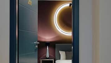 Una habitación de hotel moderna con una cama grande, una mesita de noche, una lámpara y un plafón circular en el techo.